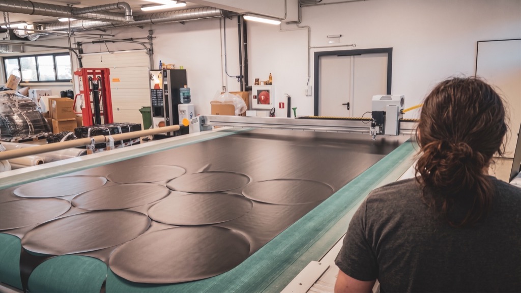 BAGJUMP technician cutting airbag topsheet material on a CNC cutter in the Austrian factory